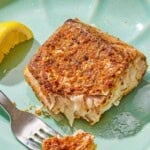 A serving of fried red snapper on a plate with a fork and a lemon wedge.