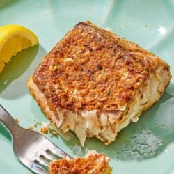A serving of fried red snapper on a plate with a fork and a lemon wedge.