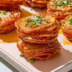A close up of potato stacks topped with chives on a sheet pan.