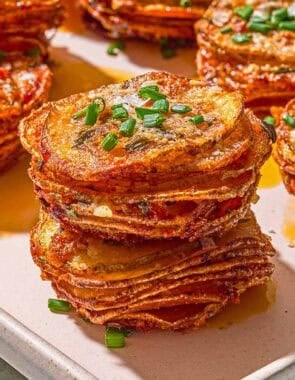 A close up of potato stacks topped with chives on a sheet pan.