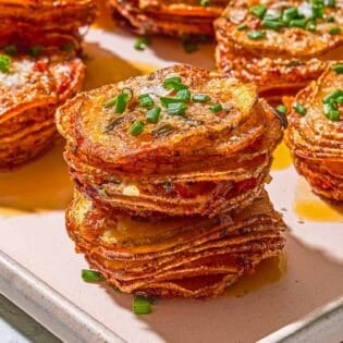 A close up of potato stacks topped with chives on a sheet pan.