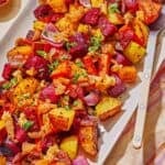 Roasted root vegetables on a platter with a serving spoon. Next to this is a bowl of aleppo pepper.