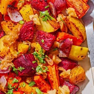 A close up of roasted root vegetables on a platter with a serving spoon.