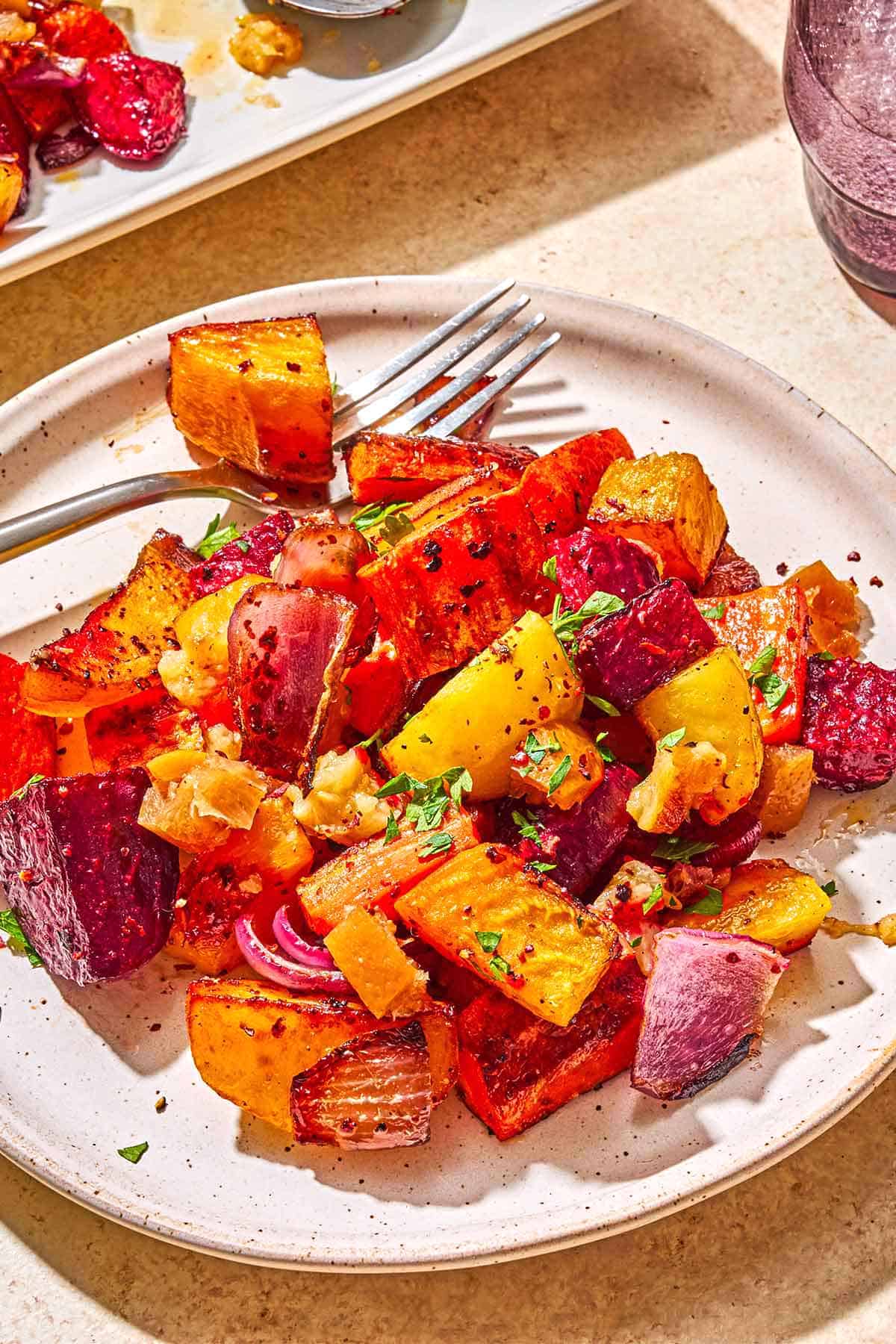 A close up of roasted root vegetables on a plate with a fork.
