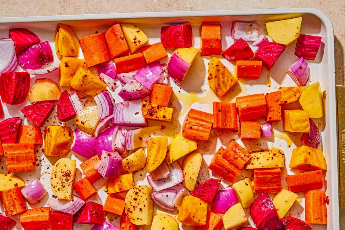 Uncooked root vegetables topped with olive oil and aleppo pepper on a sheet pan.