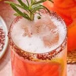 A close up of a glass of the rosemary grapefruit tonic with a grapefruit wheel, a sprig of rosemary and a sumac rim.