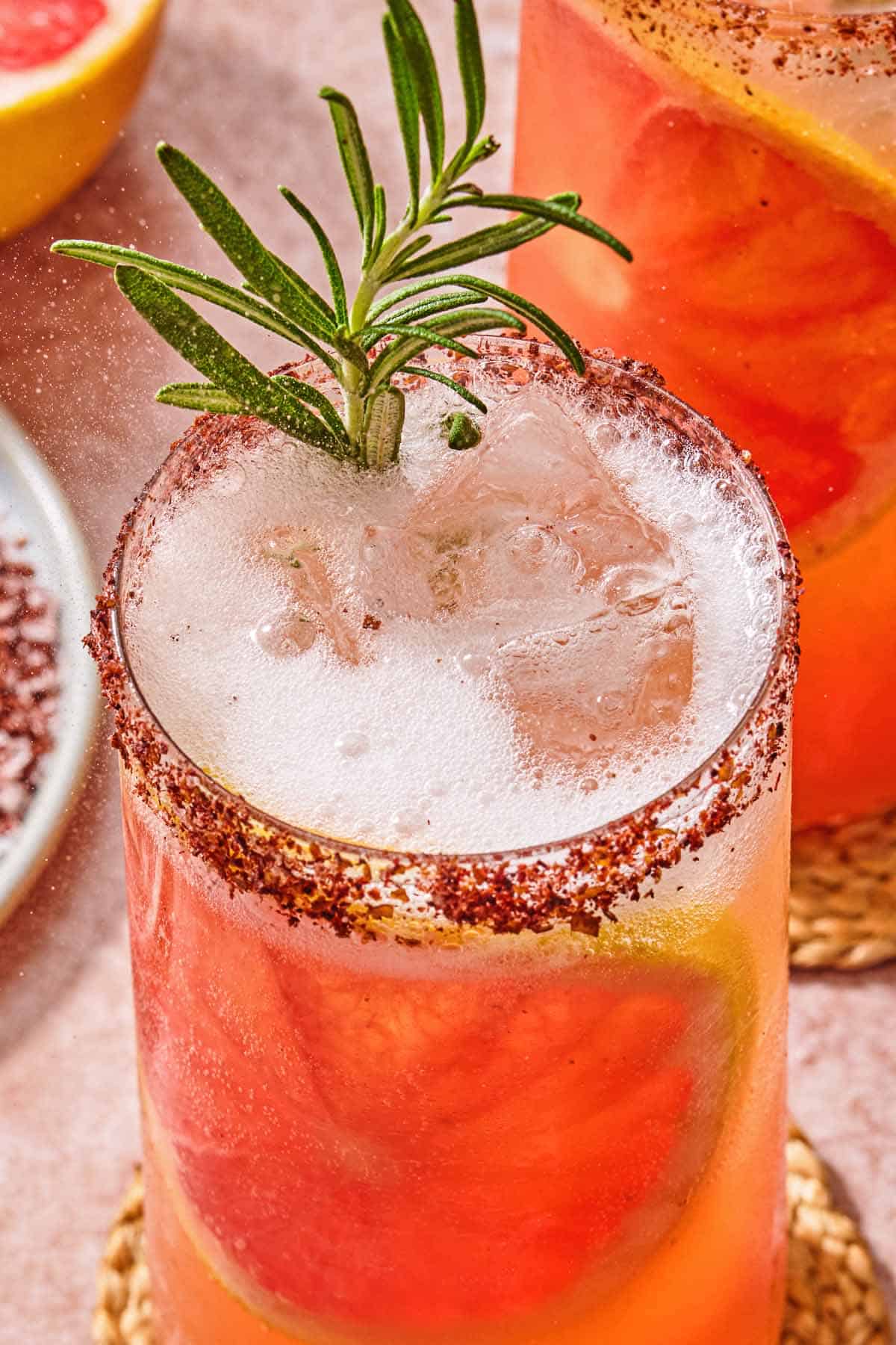A close up of a glass of the rosemary grapefruit tonic with a grapefruit wheel, a sprig of rosemary and a sumac rim.