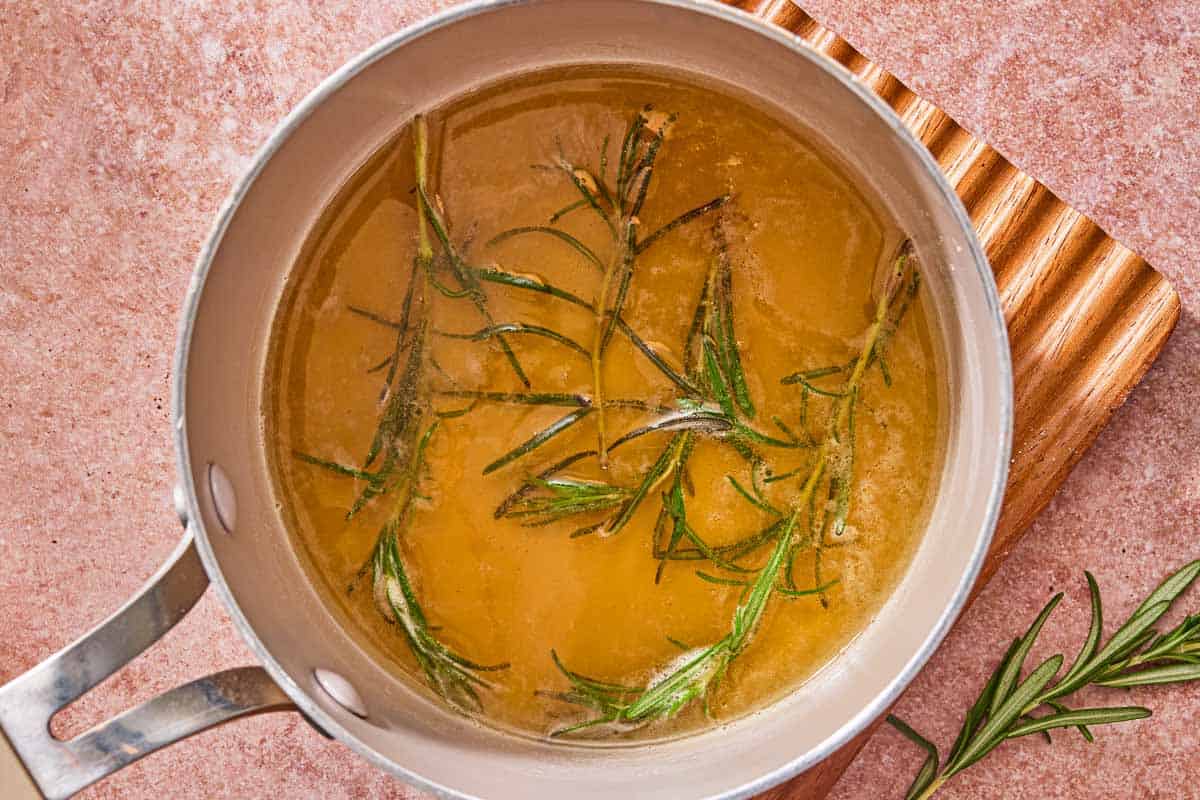 Sprigs of rosemary in a mixture of honey, water and sea salt in a sauce pan on a trivet. Next to this is a sprig of rosemary.