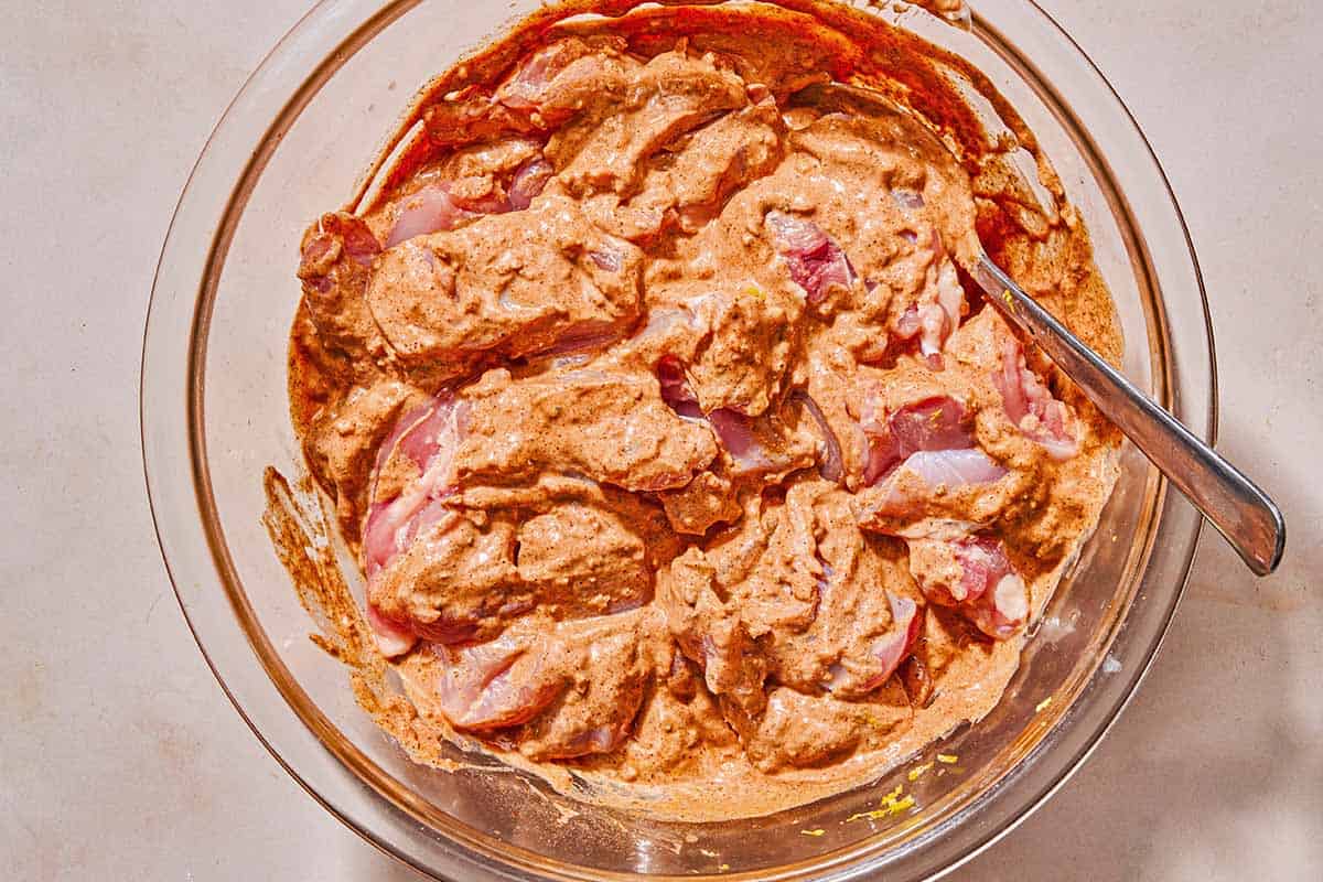 The chicken thigh pieces for the shish tawook marinading in a bowl with a spoon.