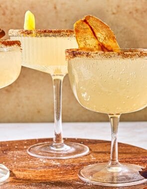 Three ginger beer mocktails on a wooden platter with a bowl of crystalized ginger pieces. In the background is another mocktail.