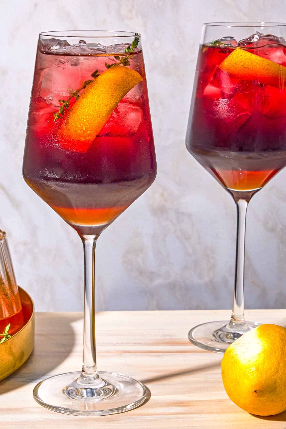 Two tart cherry juice mocktails garnished with lemon twists and sprigs of fresh thyme.