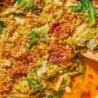 An overhead photo of utica greens in a skillet with a wooden spoon.