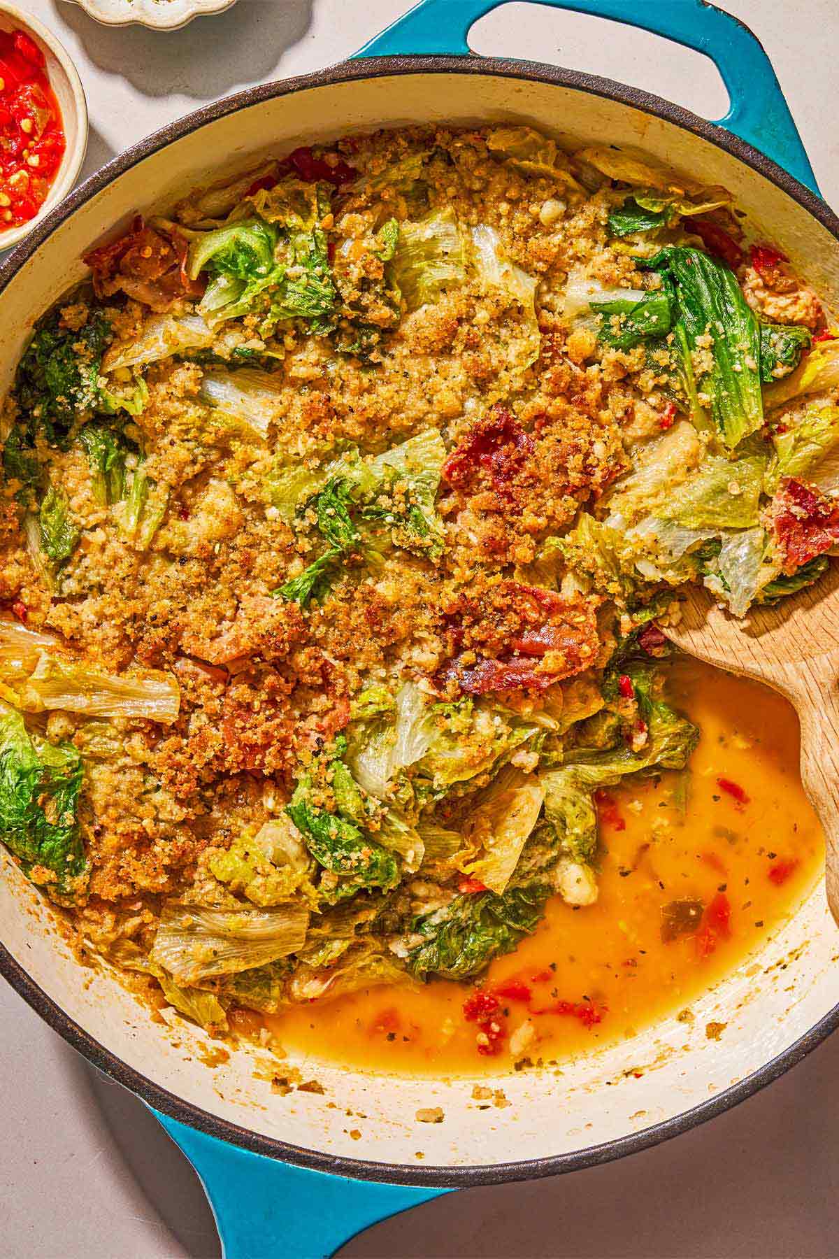 An overhead photo of utica greens in a skillet with a wooden spoon.