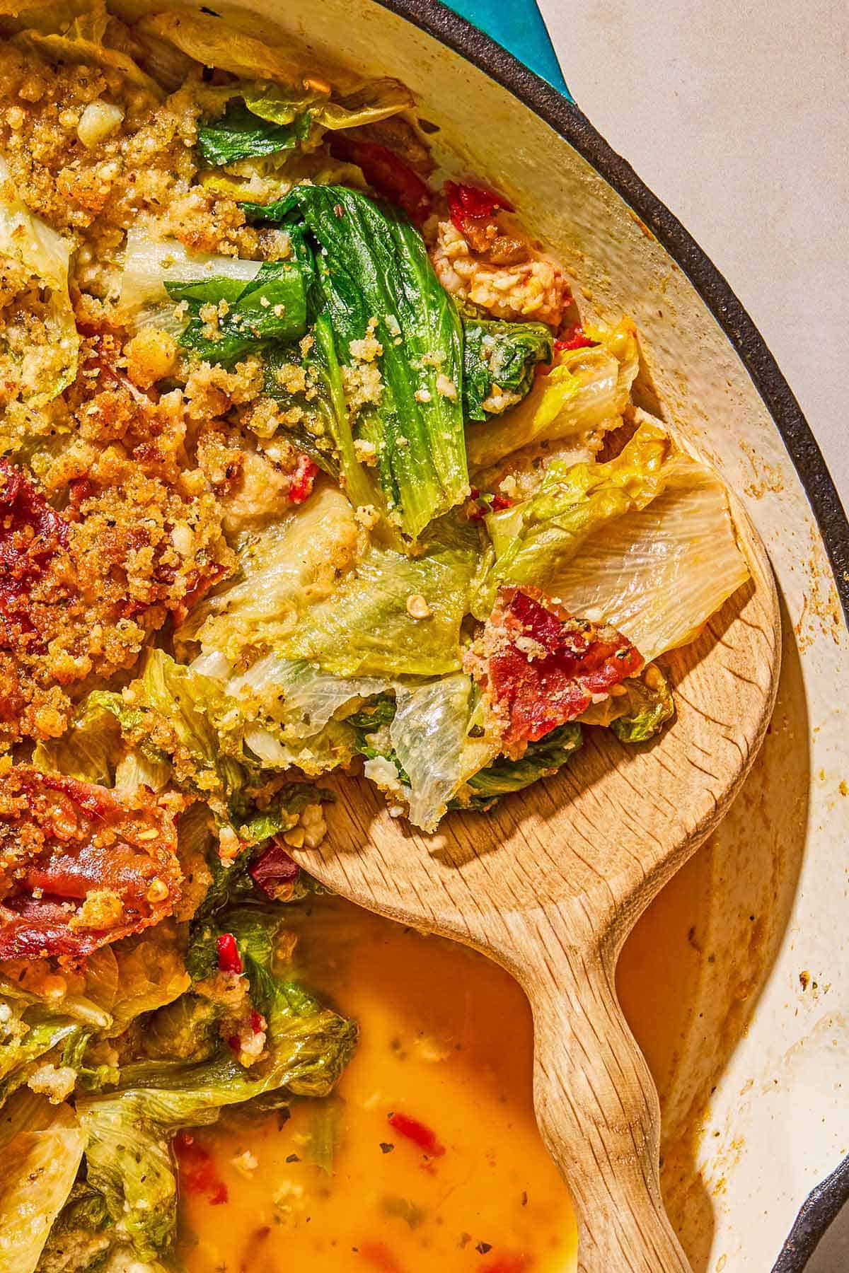 A close up of utica greens in a skillet with a wooden spoon.