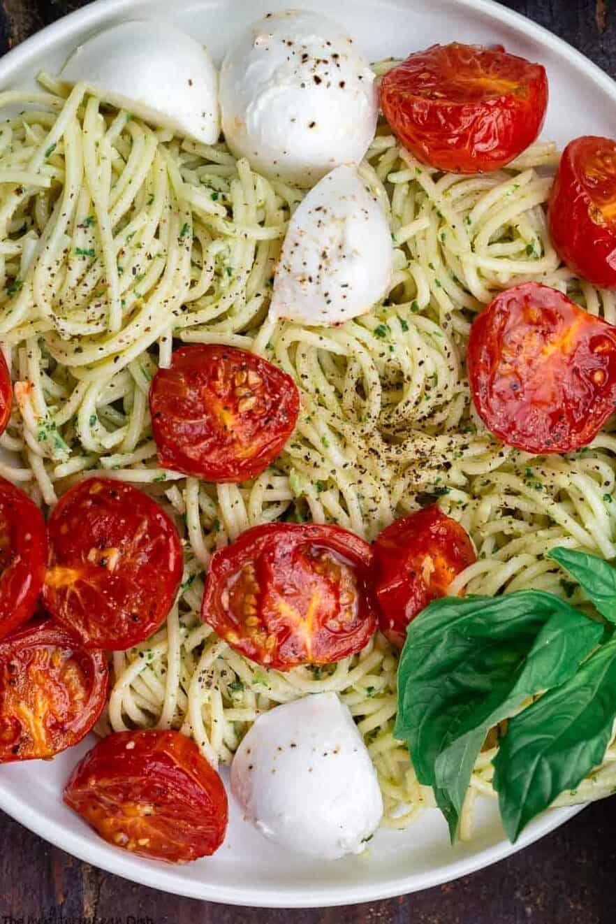 pesto pasta on two plates with a side of fresh basil