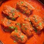 The braciole braised in marinara sauce in a cast iron skillet.