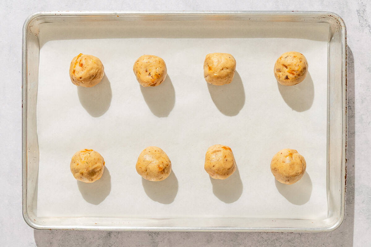 Dough balls for the apricot cookies on a parchment lined sheet pan.