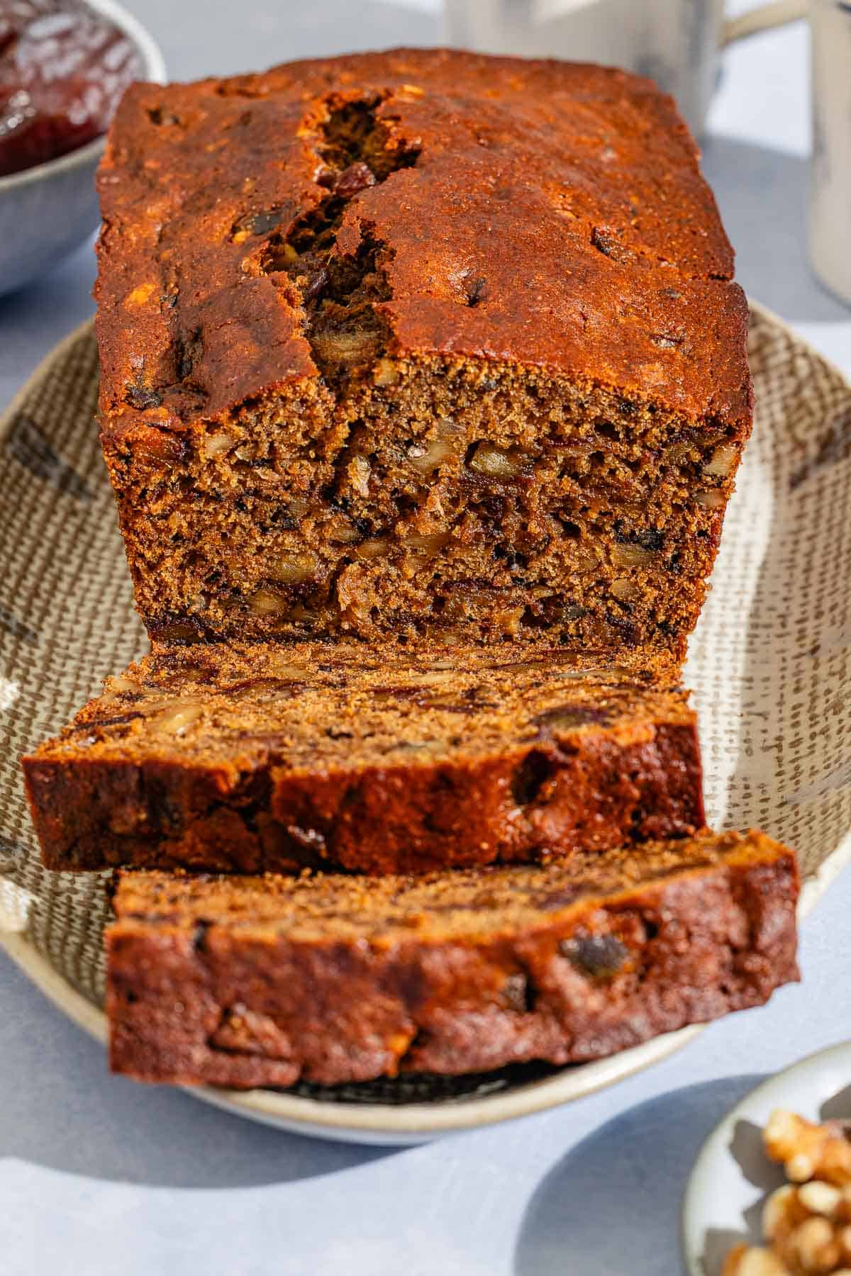 A partially sliced loaf of date nut bread behind 2 slices of the bread on a platter.