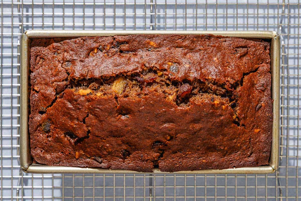 The date nut bread in a loaf pan cooling on a wire rack.