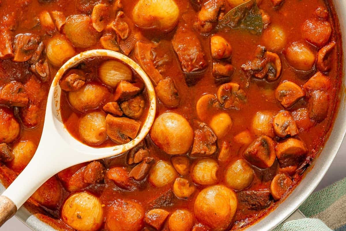The mushroom stew in a tall sided skillet with a ladle.