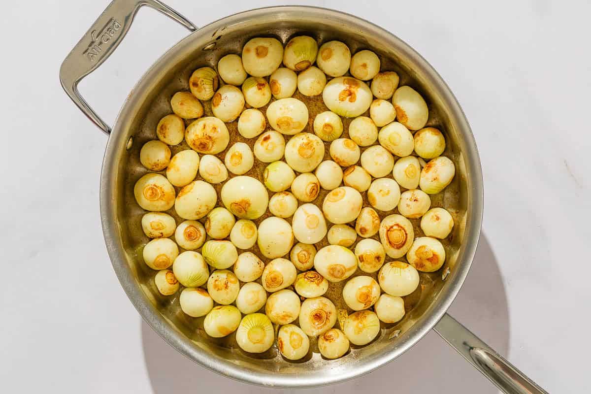 Pealed pearl onions being seared in a tall sided skillet.