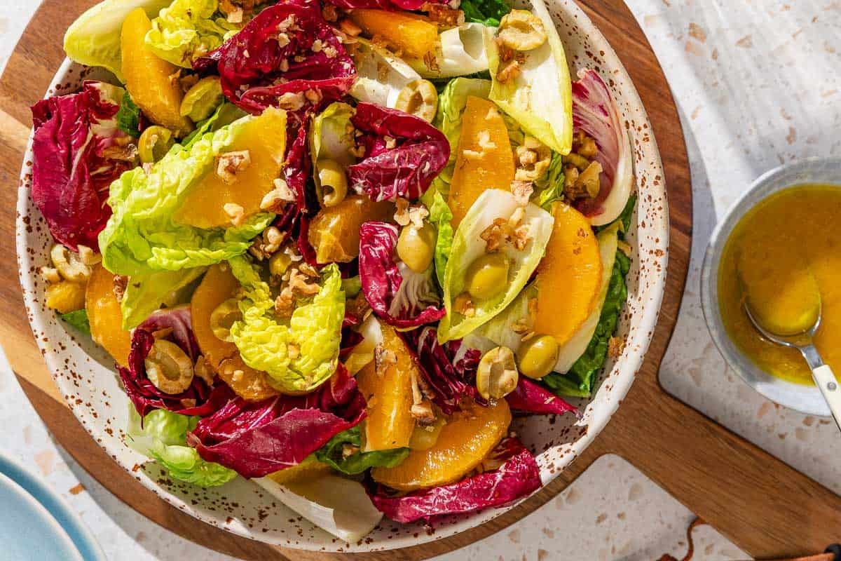 Orange salad in a serving bowl on a wooden tray next to a bowl with the orange vinaigrette with a spoon.