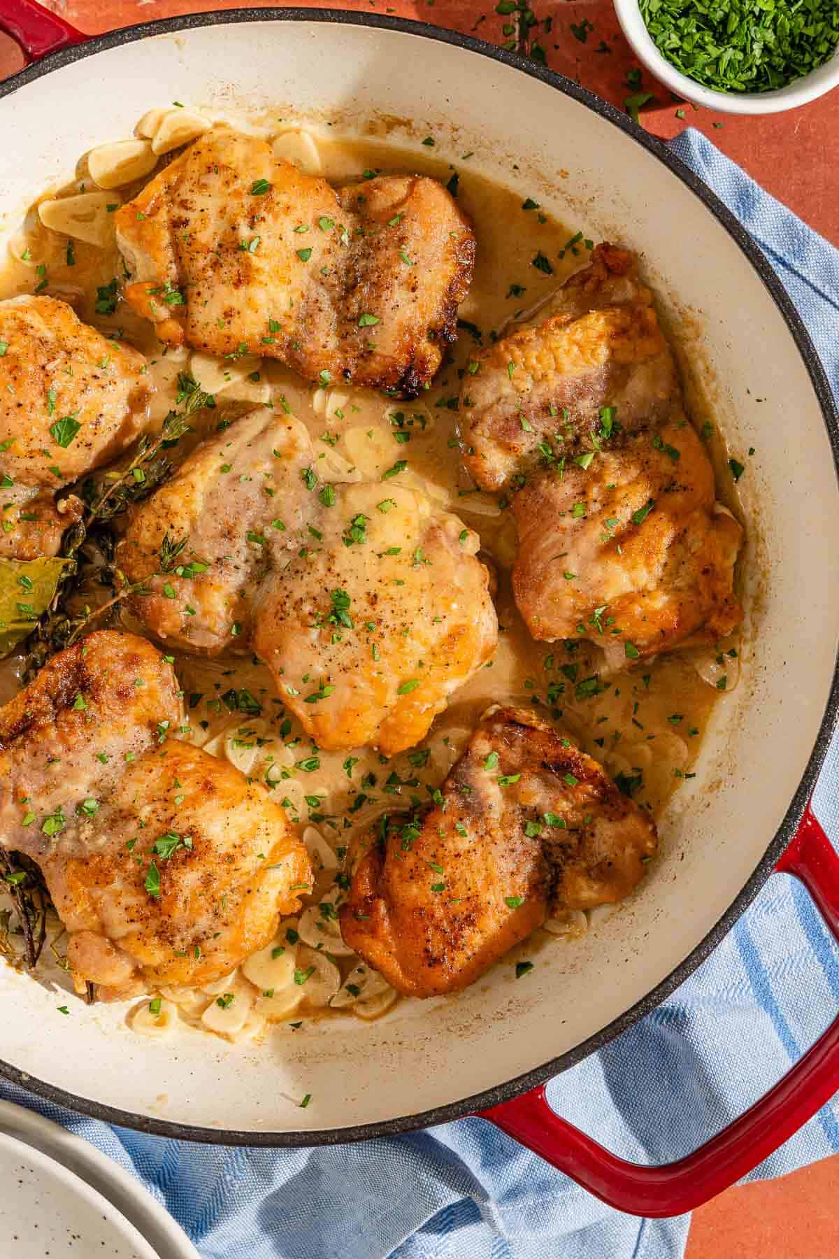 Spnaish garlic chicken recipe (Pollo al Ajillo) in a skillet next to a bowl of chopped parsley.