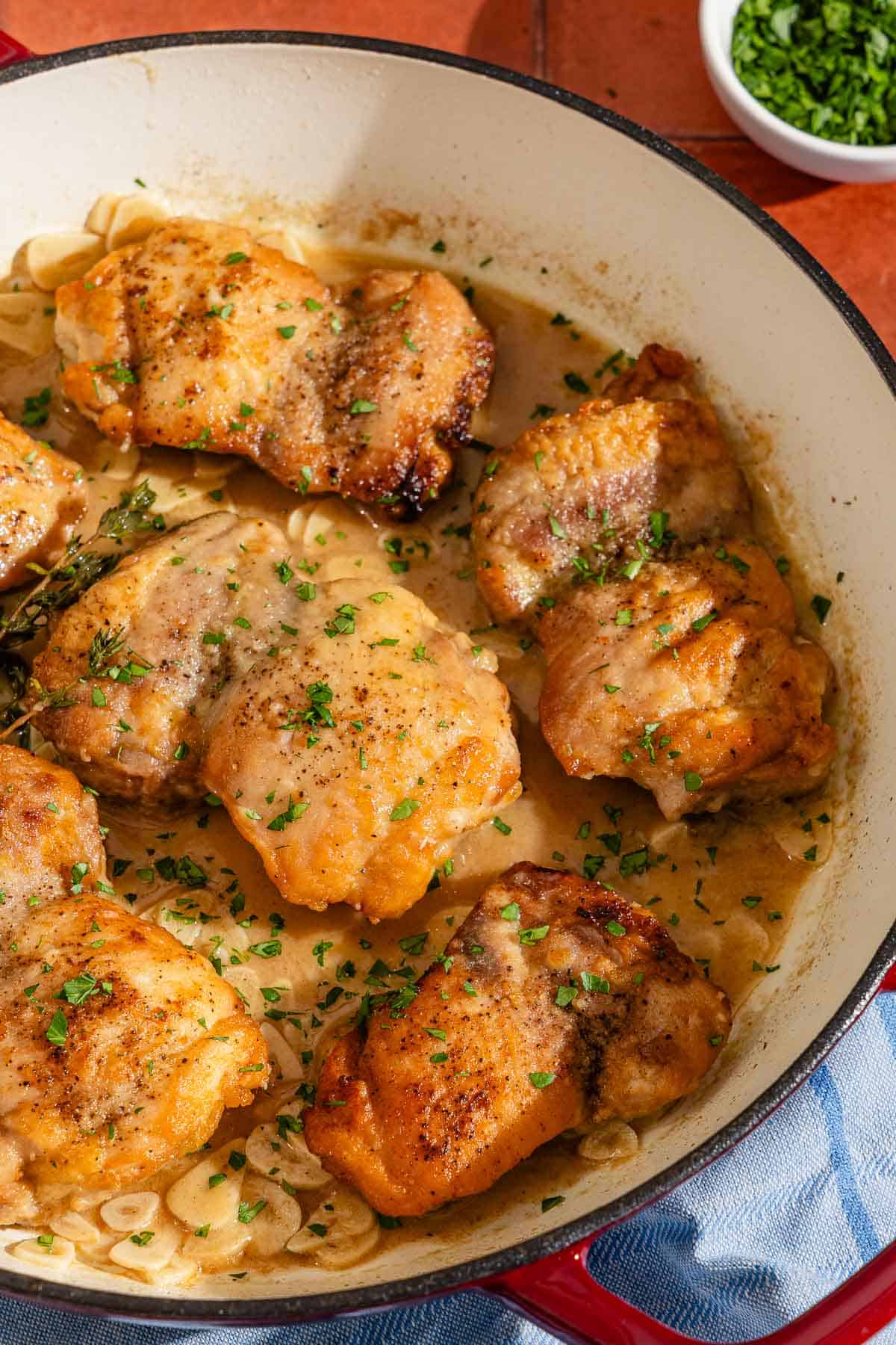 The garlic chicken recipe in a skillet next to a bowl of chopped parsley.