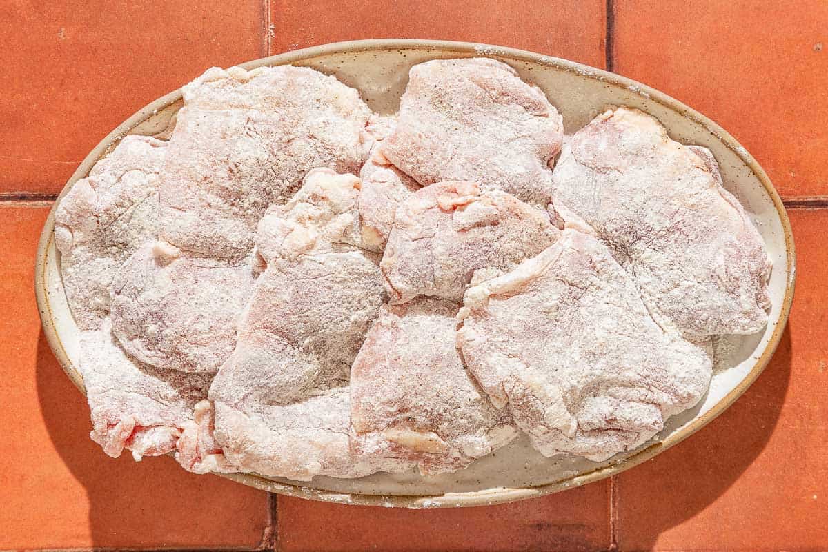 The seasoned and flour coated chicken thighs for the garlic chicken recipe on a platter.