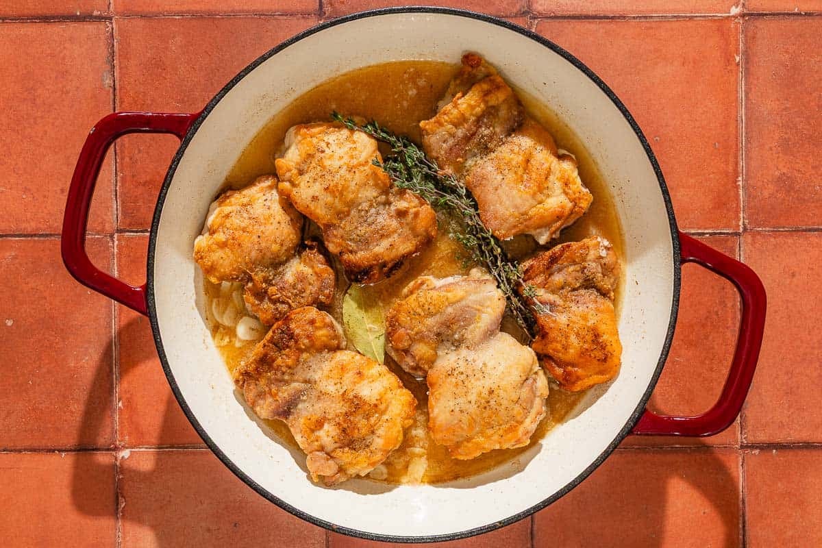The chicken thighs for the garlic chicken recipe being cooked in sauce in a skillet.