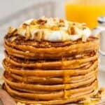 A stack of gluten free sweet potato pancakes topped with labneh, nuts and honey on a plate with a fork.