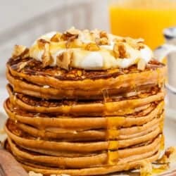 A stack of gluten free sweet potato pancakes topped with labneh, nuts and honey on a plate with a fork.