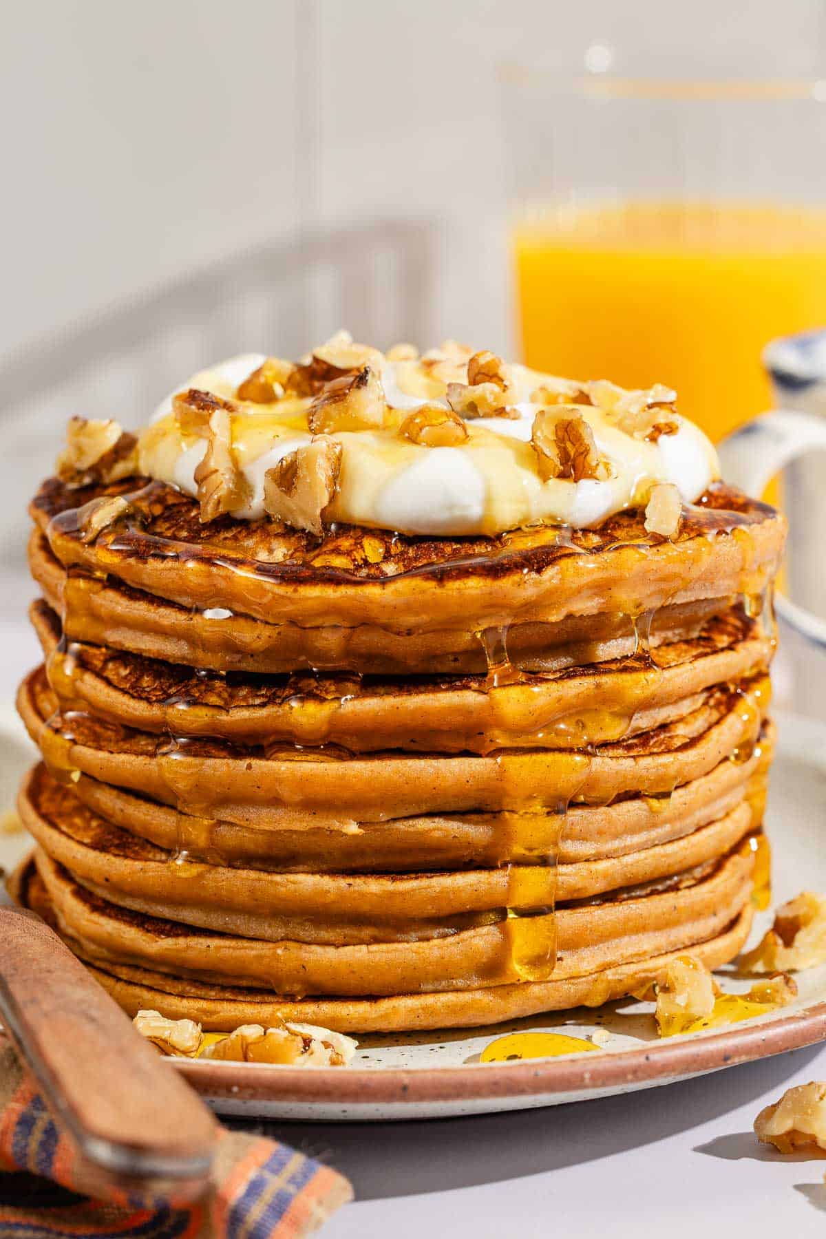 A stack of gluten free sweet potato pancakes topped with labneh, nuts and honey on a plate with a fork.