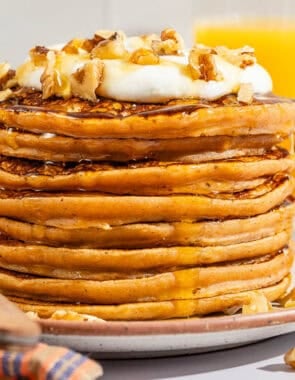 A stack of gluten free sweet potato pancakes topped with labneh, nuts and honey on a plate with a fork.