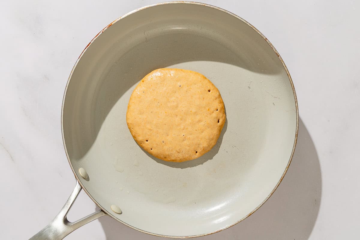 A sweet potato pancake being cooked in a skillet.