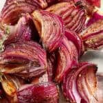 Roasted red onions on a platter with a serving spoon.