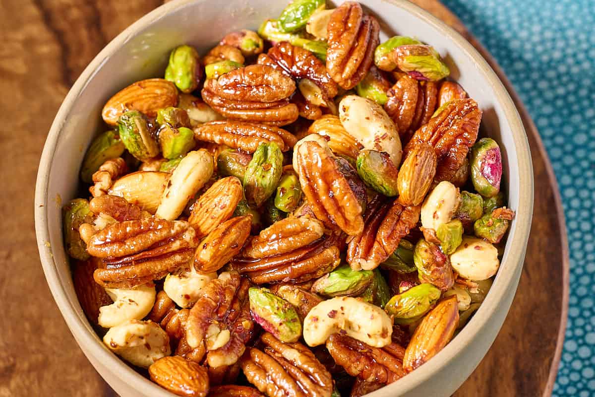 Spiced nuts in a bowl on a wooden tray.