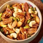 Spiced nuts in a bowl on a wooden tray.