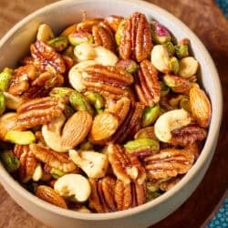Spiced nuts in a bowl on a wooden tray.