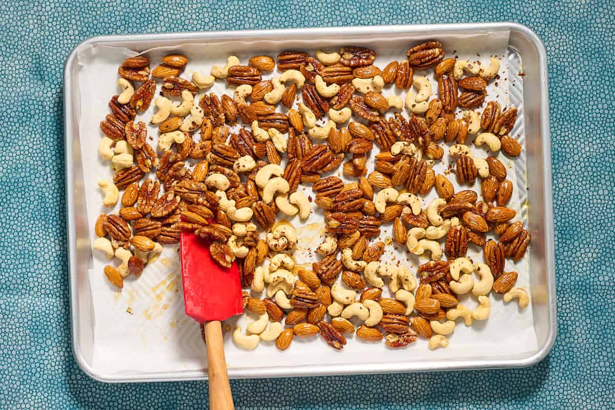 The spiced nuts recipe being stirred with a spatular on a parchment lined sheet pan.