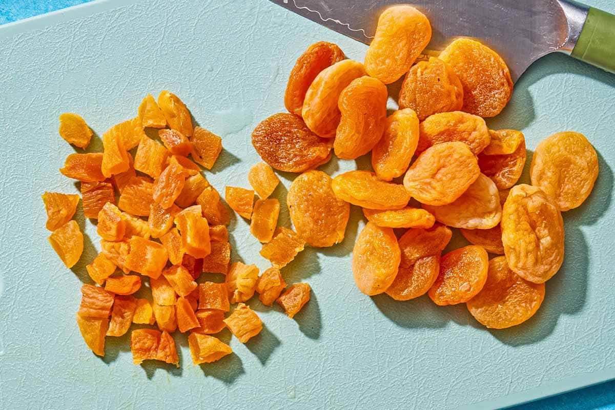Whole dried apricots and chopped dried apricots on a cutting board with a knife.