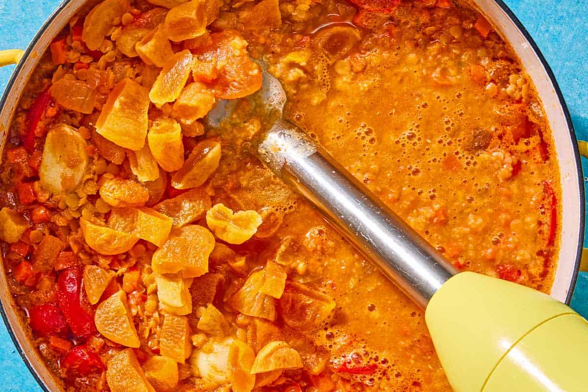 The red lentil soup being in a pot being blended with an immersion blender.