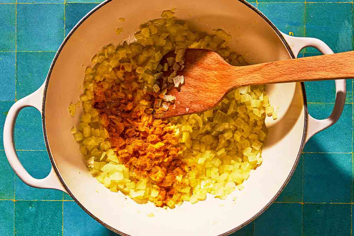 The onions and turmeric for the beet soup being sautéed in a pot with a wooden spatula.