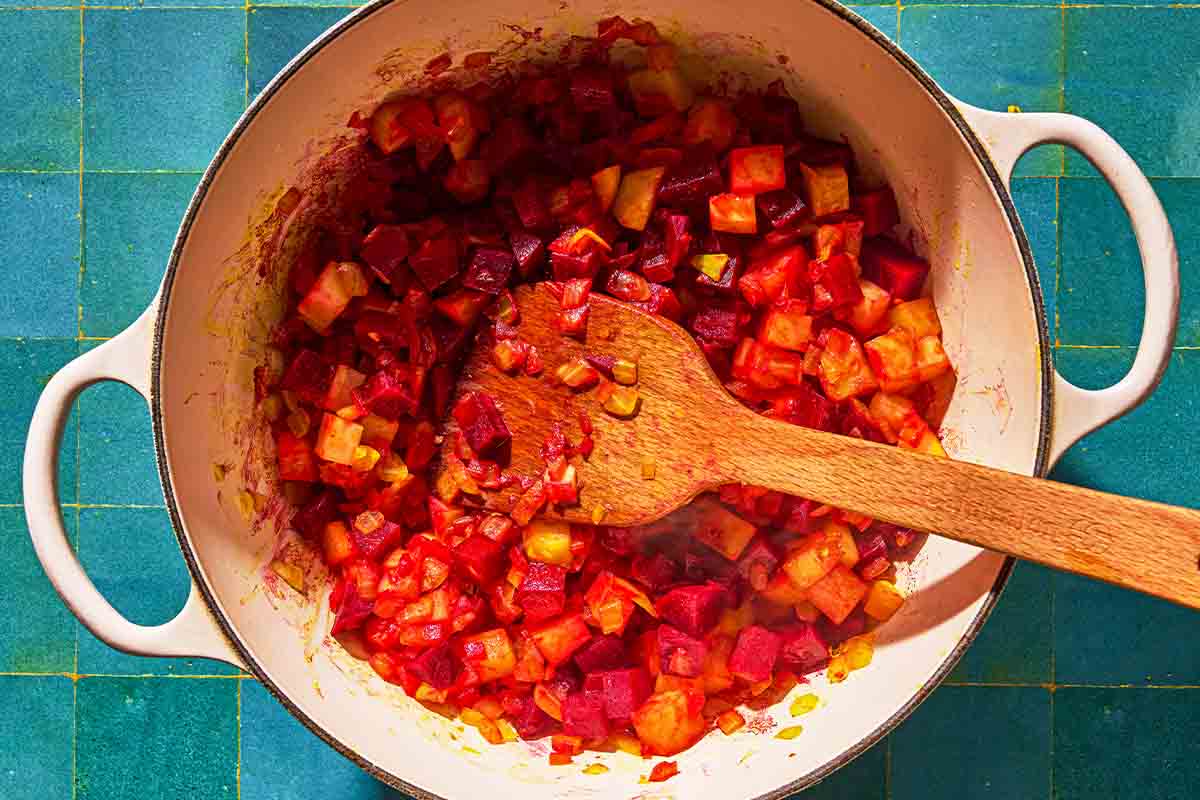 The beets and potato added to the onion mixture in a large pot with a wooden spatula.