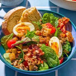 A breakfast salad in a bowl with toast next to a small pitcher with the red wine vinaigrette.
