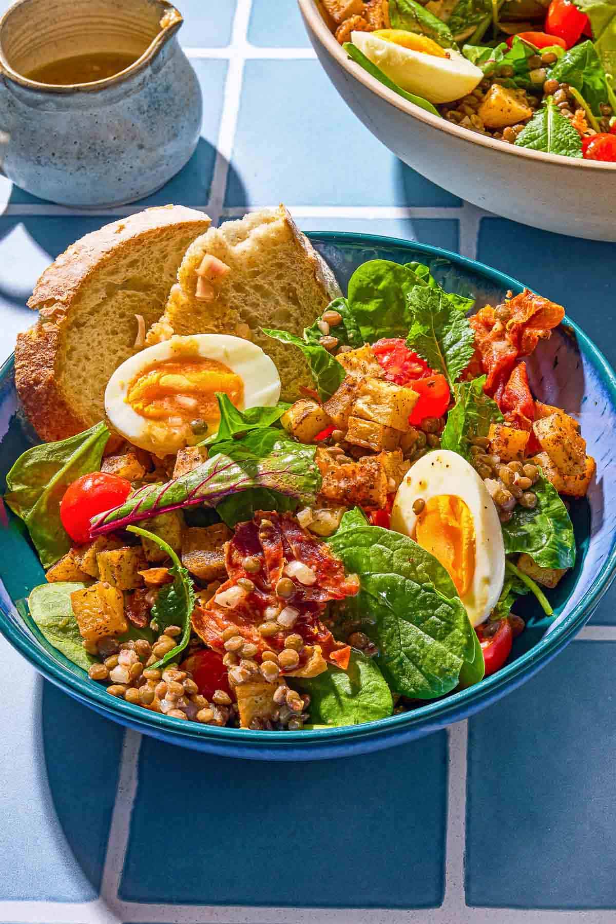 A breakfast salad in a bowl with toast next to a small pitcher with the red wine vinaigrette.