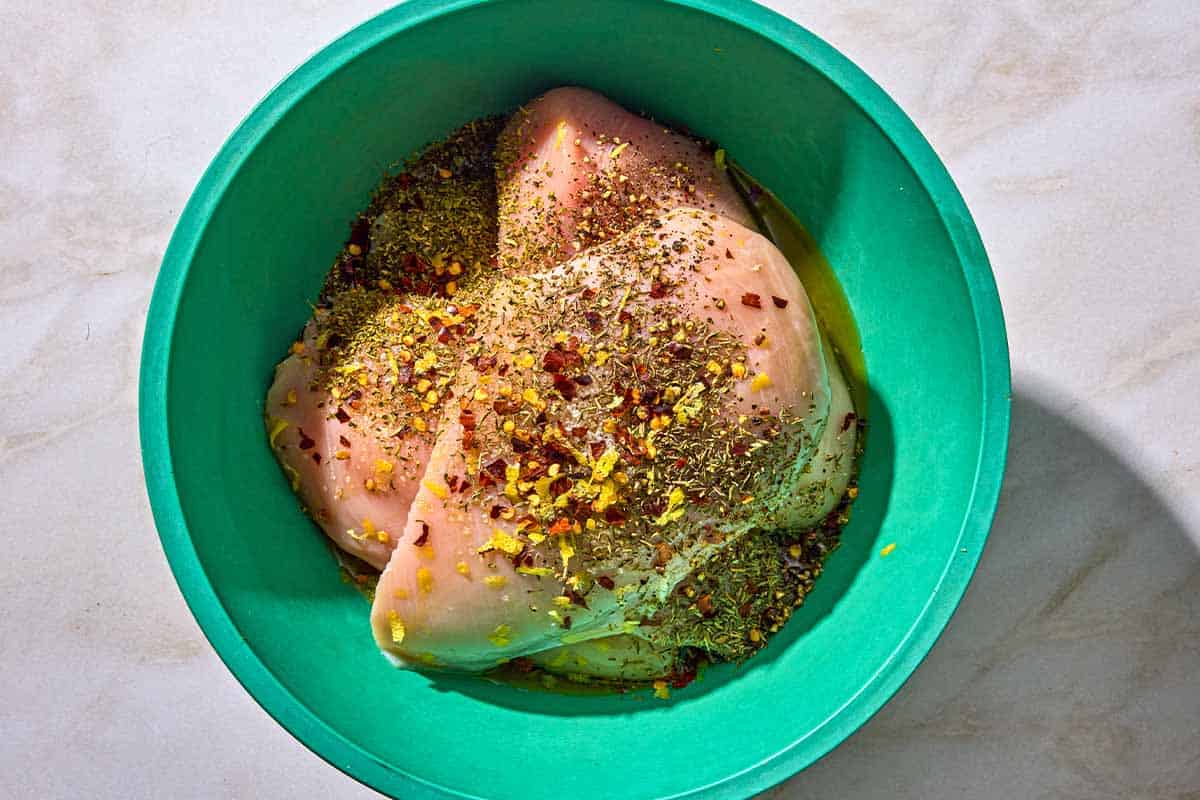 The chicken breasts for the chicken and broccoli recipe in a bowl with olive oil and spices.