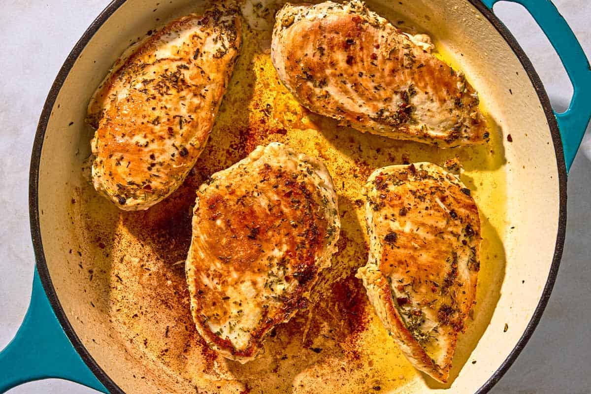 Four chicken breasts being browned in a skillet.