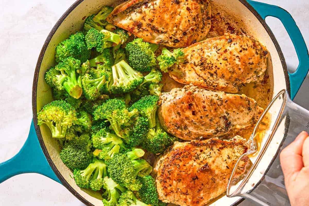 Water being poured into a skillet with the chicken and broccoli.
