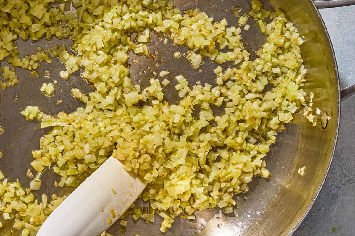 The chopped fennel, garlic and shallot for the phyllo cup appetizers being sauteed in a skillet with a spatula.